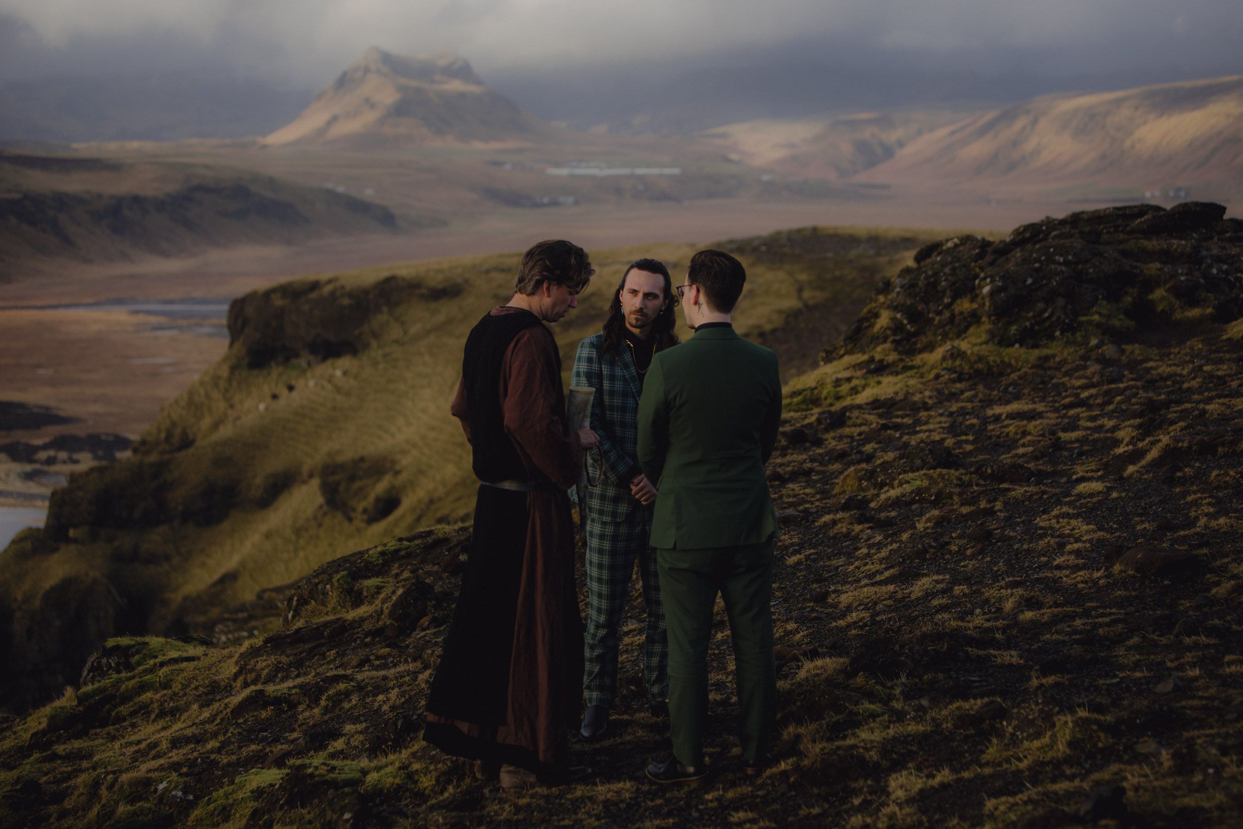 Three people admire a scenic mountain landscape from a hilltop viewpoint.