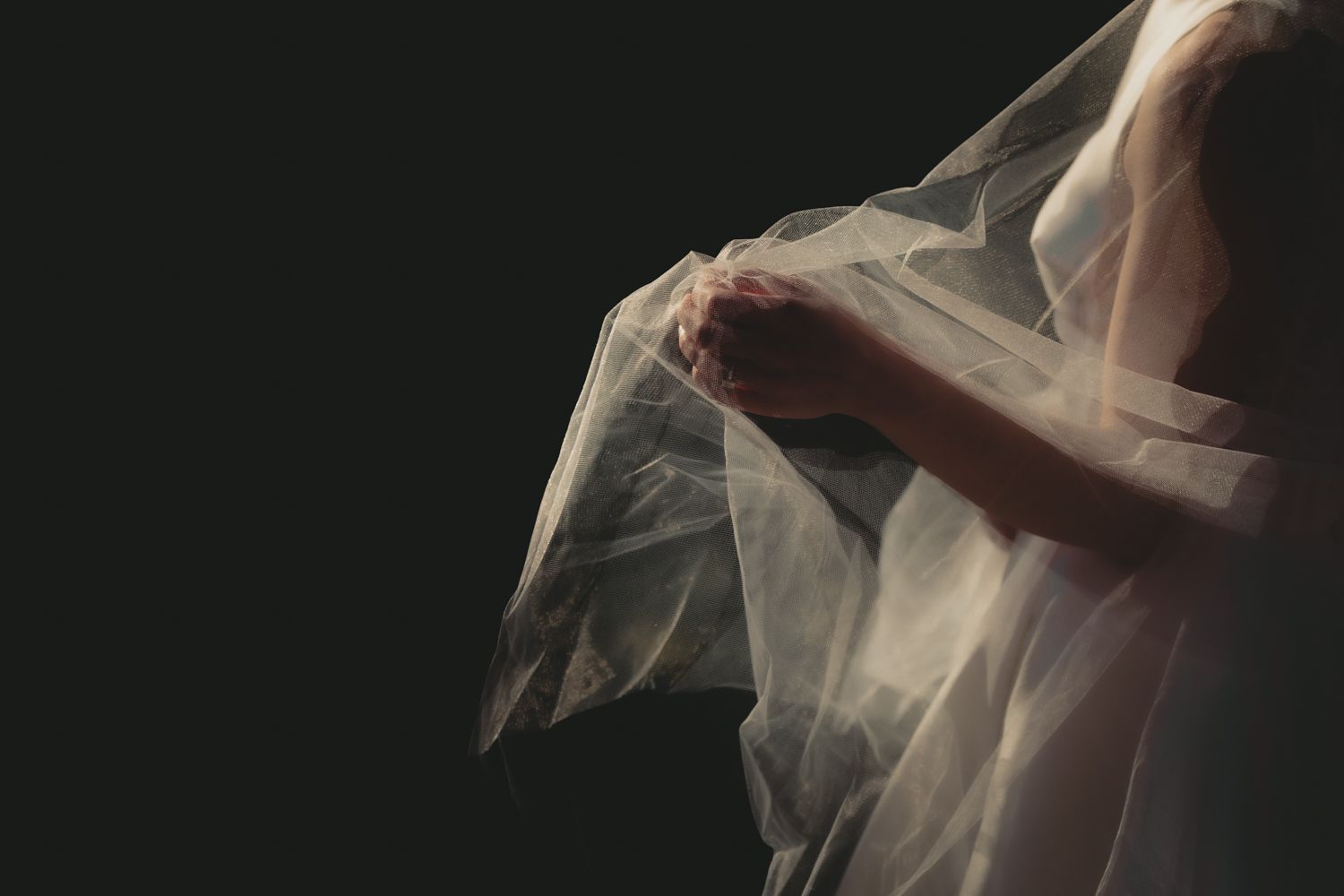 Delicate sheer wedding veil flowing gracefully against dark background.
