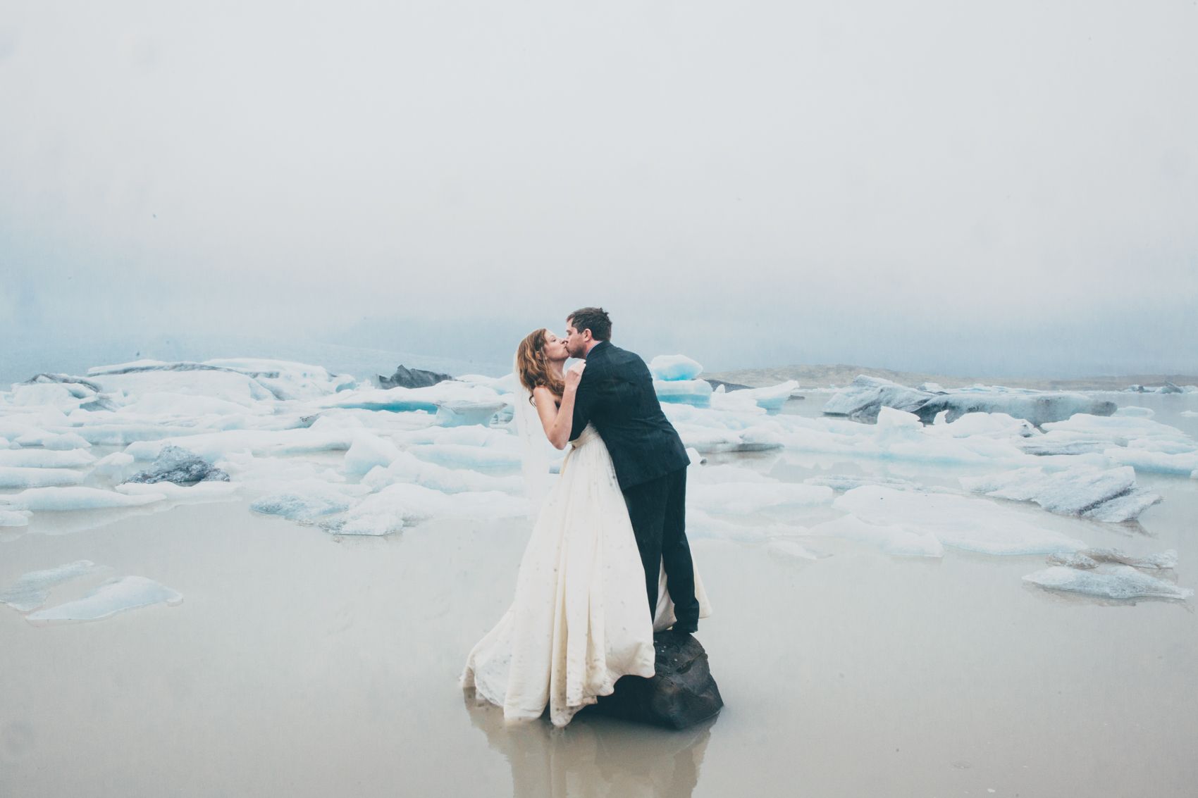 A romantic moment captured on an icy beach with glaciers and fog in the background.