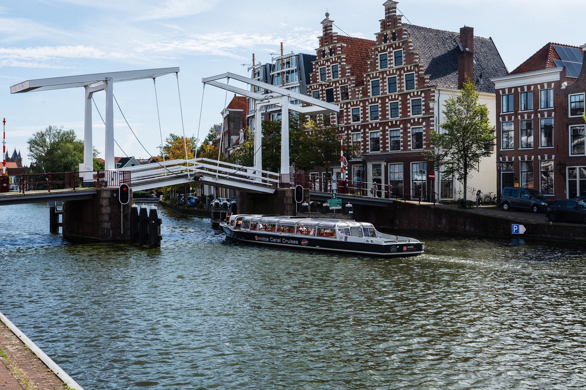 A tour boat cruises along a Dutch canal past a white drawbridge and historic step-gabled buildings in Haarlem, Netherlands.