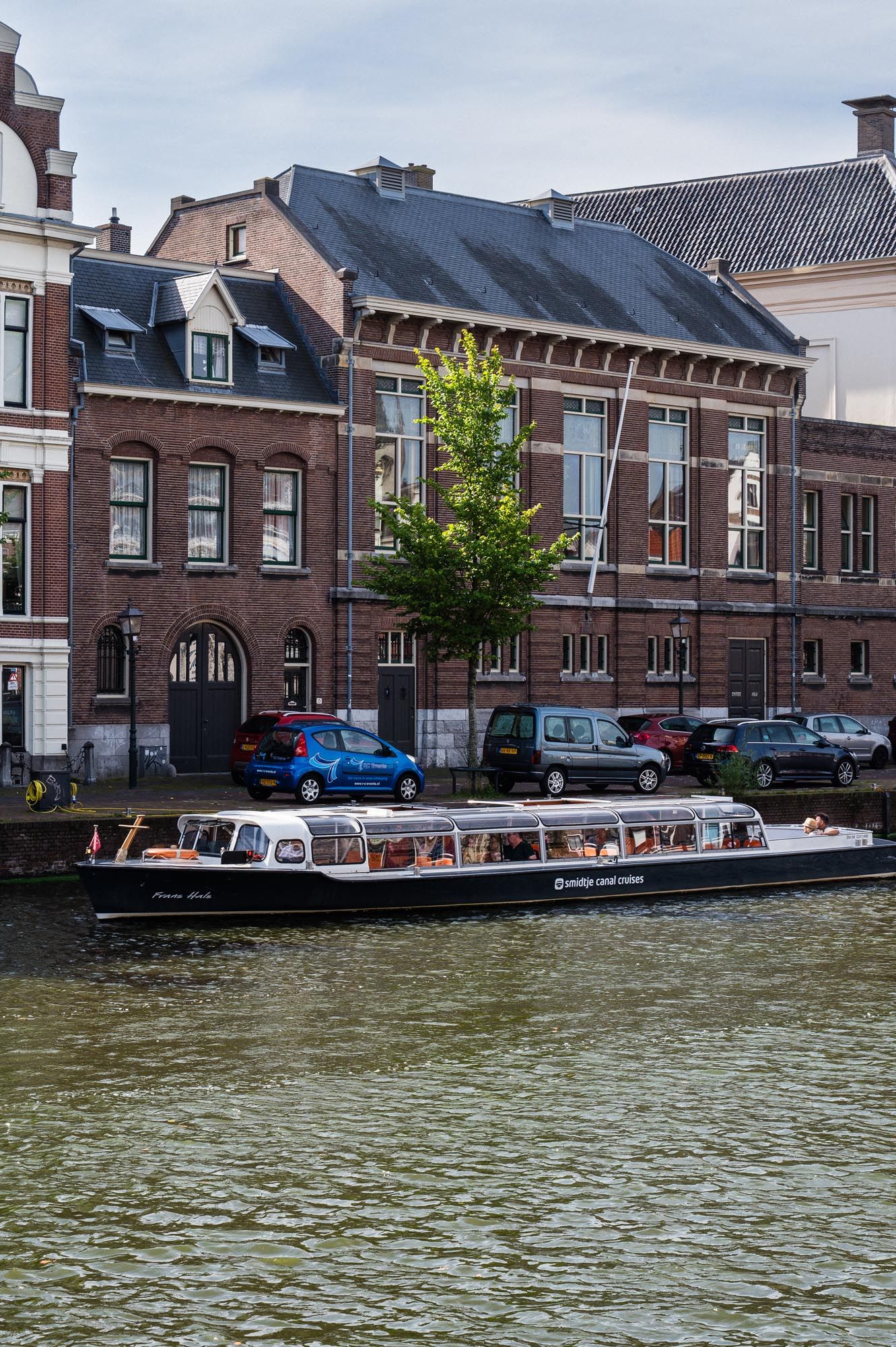 A tour boat cruises along a canal in front of historic Dutch brick buildings in the Netherlands.