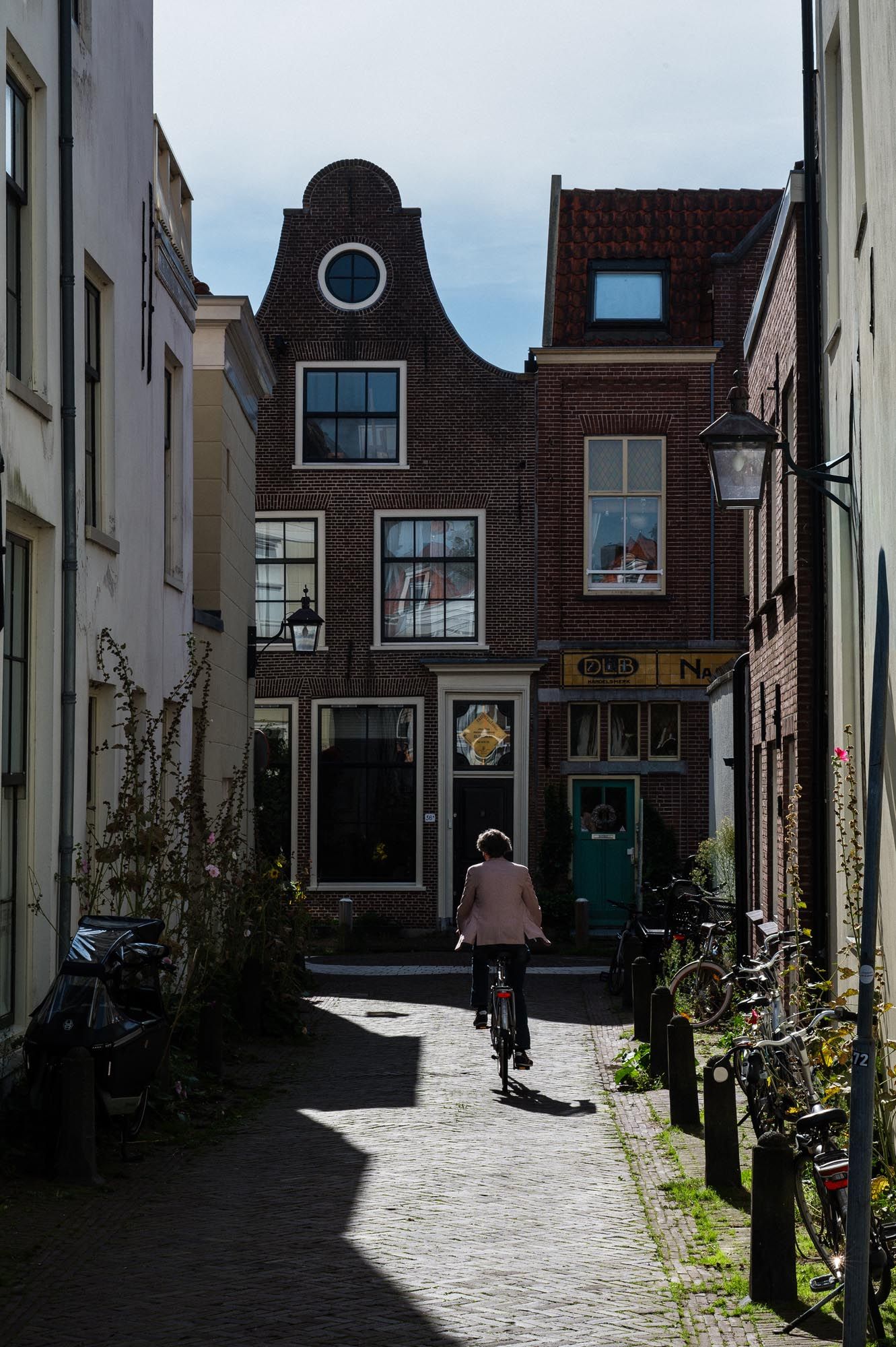 Person cycling through a narrow cobblestone alley lined with traditional Dutch brick buildings on a sunny day.