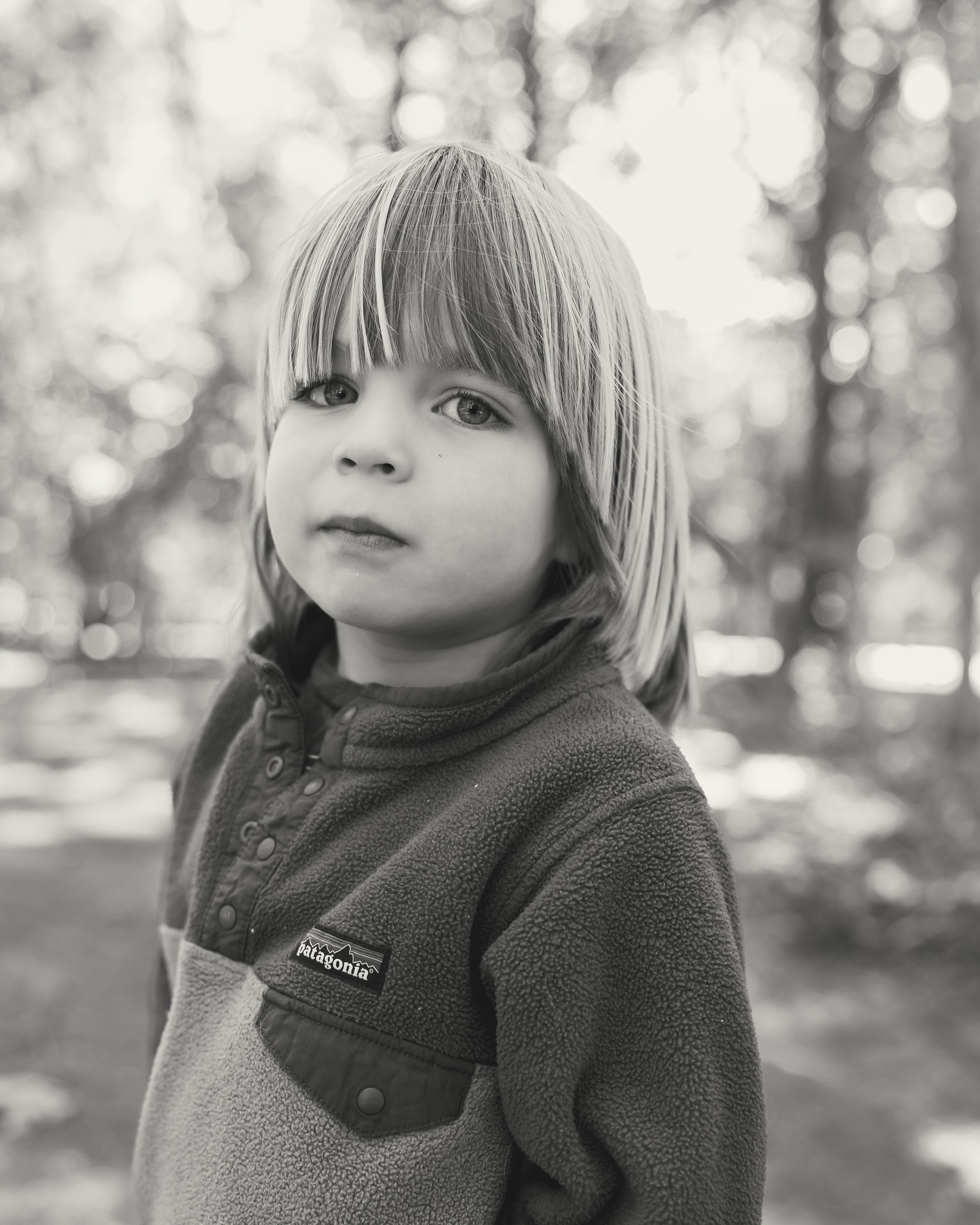 Black and white portrait of a young child with blonde hair wearing a Patagonia fleece jacket outdoors.