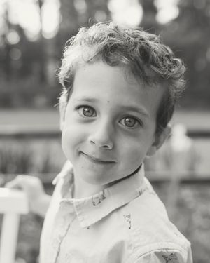 Black and white portrait of a young curly-haired child smiling softly outdoors.