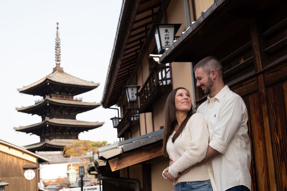 Smiling couple embracing on a traditional wooden street in Kyoto with the Yasaka Pagoda rising in the background at sunset.