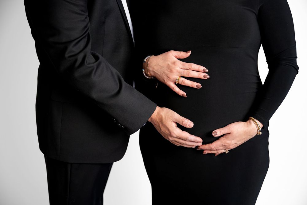 Close-up of expecting couple's hands gently cradling pregnant belly in matching black outfits.