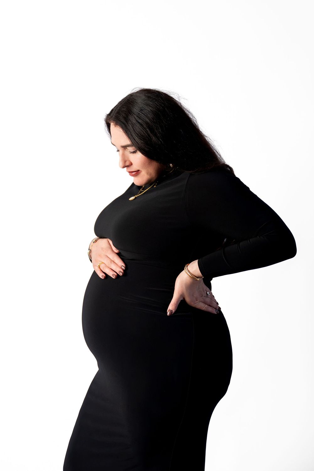 Pregnant woman in black dress cradling baby bump on white background.