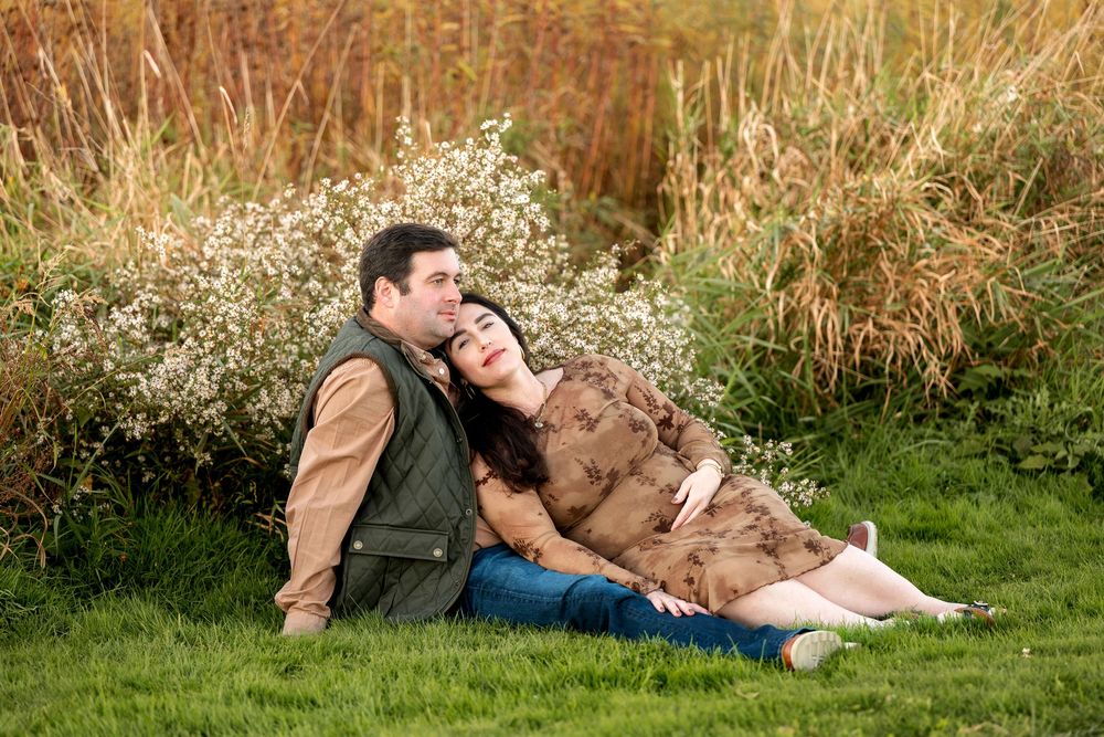 Couple sitting together on grass surrounded by wildflowers during golden hour maternity photo session.