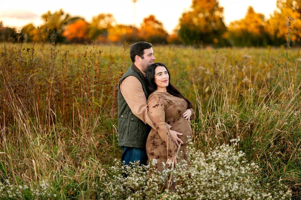 Couple embracing in golden autumn field with wildflowers and warm sunset light filtering through tall grass.