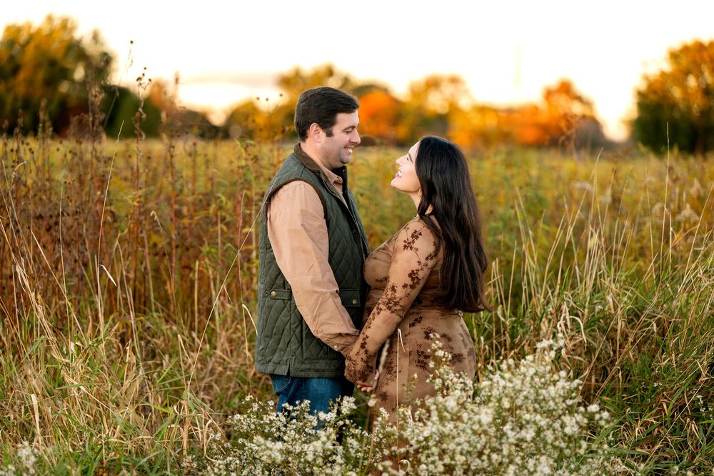 Couple holding hands and smiling at each other in a golden autumn field at sunset.