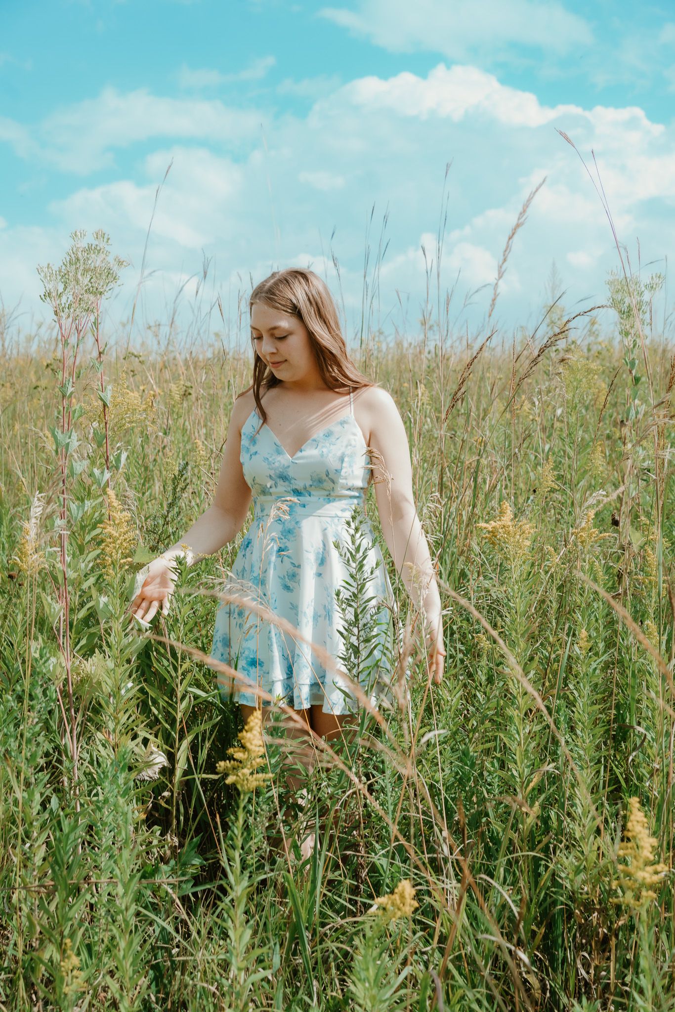 Dreamy summer portrait of someone in light blue dress standing among tall wildflowers.