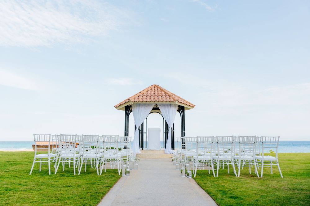 Oceanfront wedding gazebo with white draped curtains and rows of white chairs along a stone aisle on a green lawn overlooking the sea.