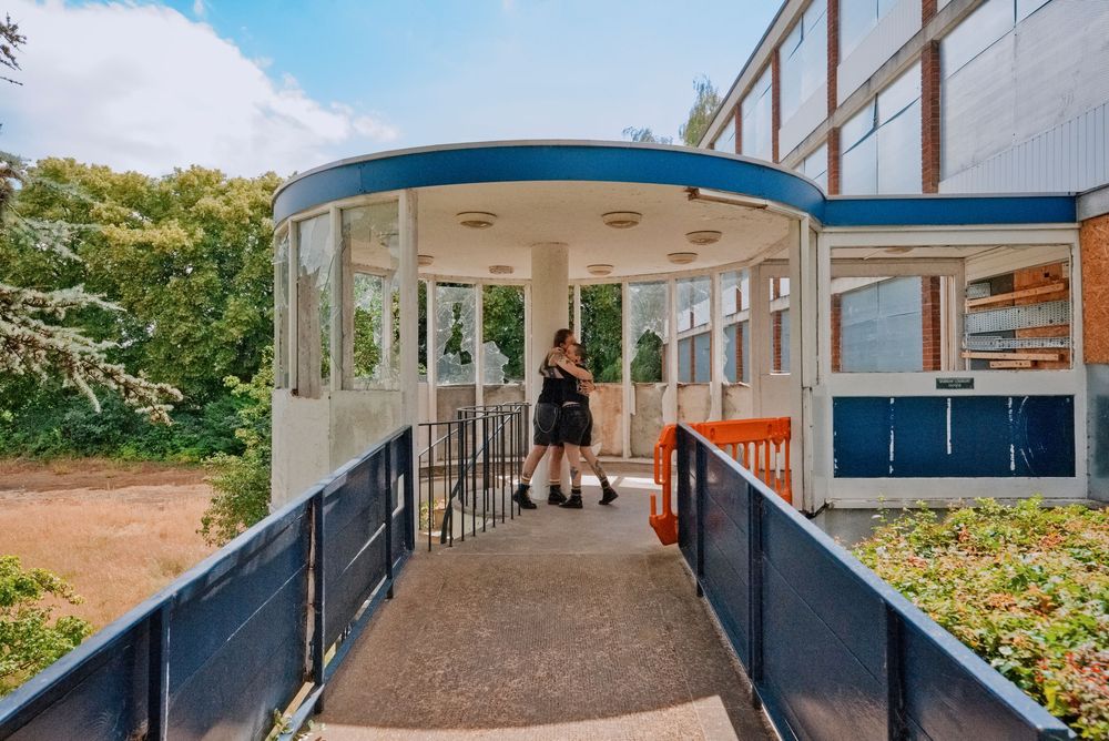 A student walks up a ramp leading to a modern circular school entrance with large windows on a sunny day.