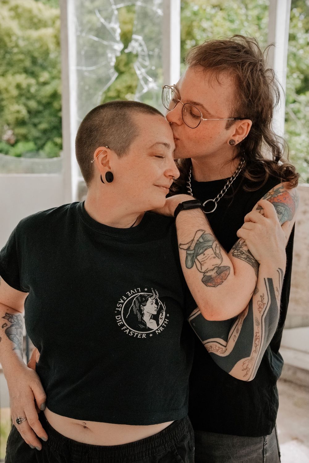 Two tattooed people sharing a tender kiss, both wearing black t-shirts.
