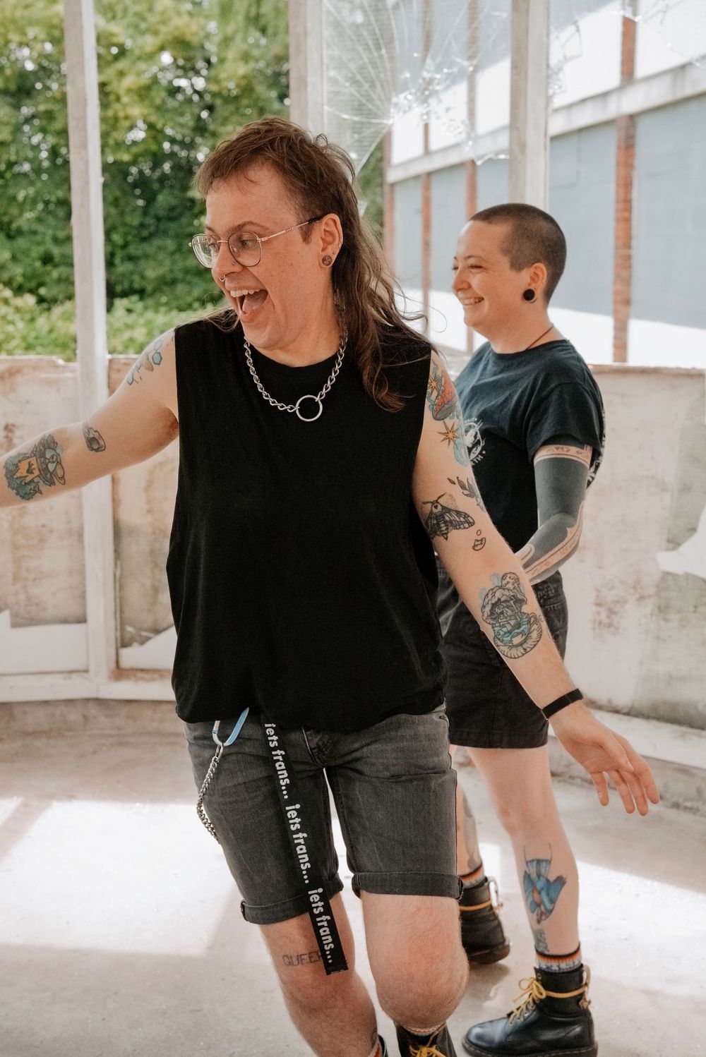 Two tattooed individuals laughing and dancing in a bright, airy space.