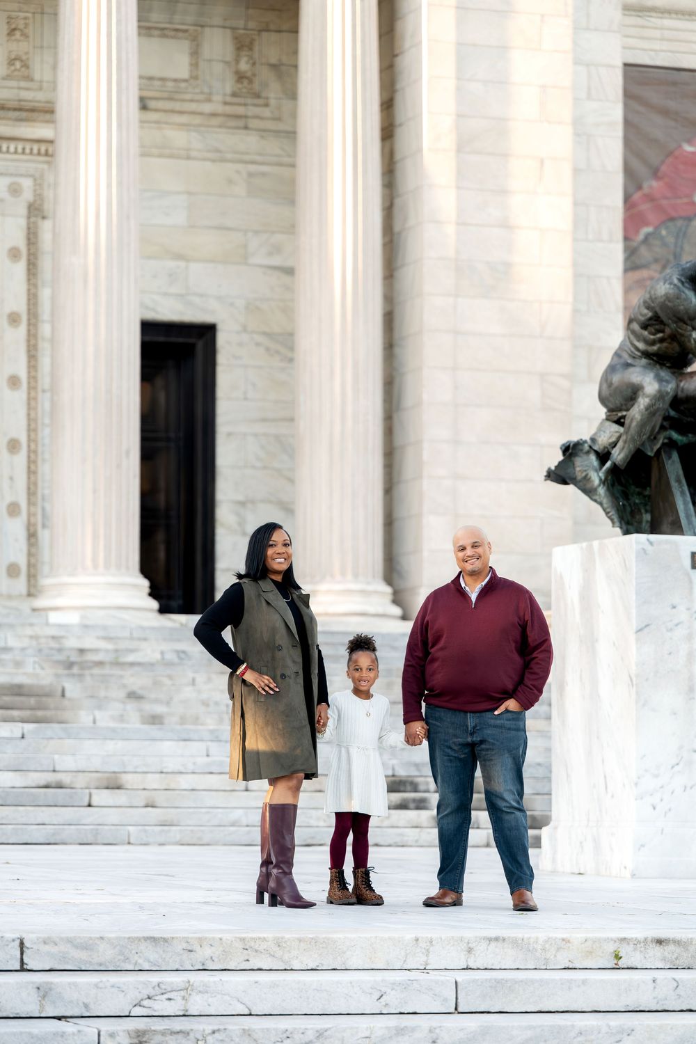 A family of three poses on marble steps in front of a classical building with columns.