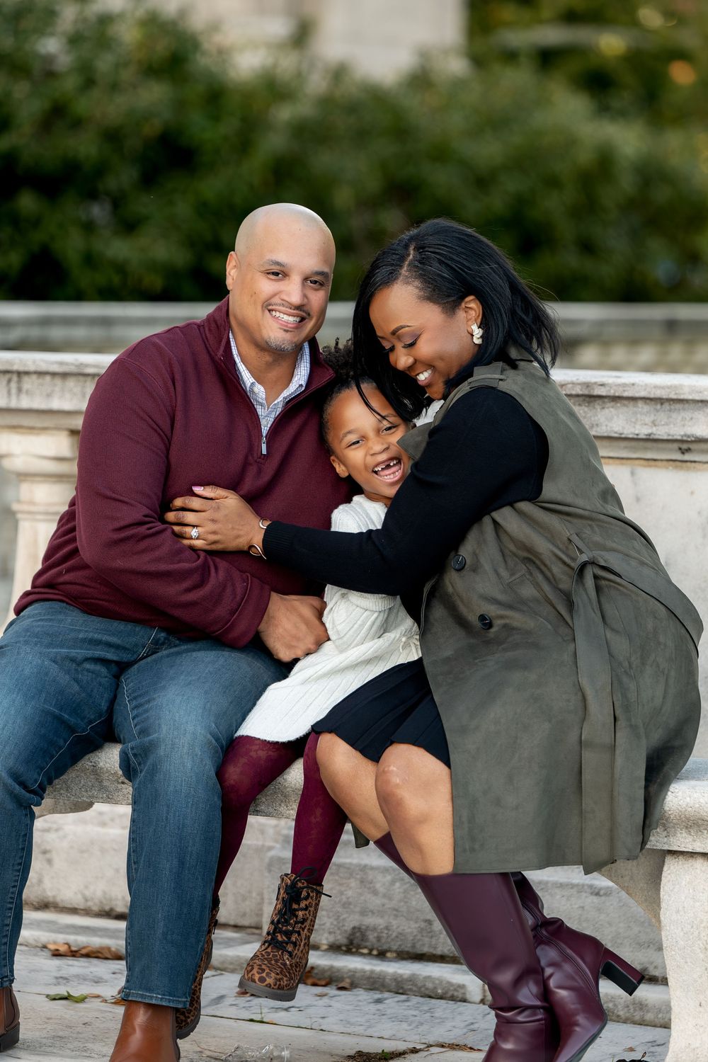 Happy family of three sharing a warm embrace while sitting on stone steps during a fall outdoor photo session.