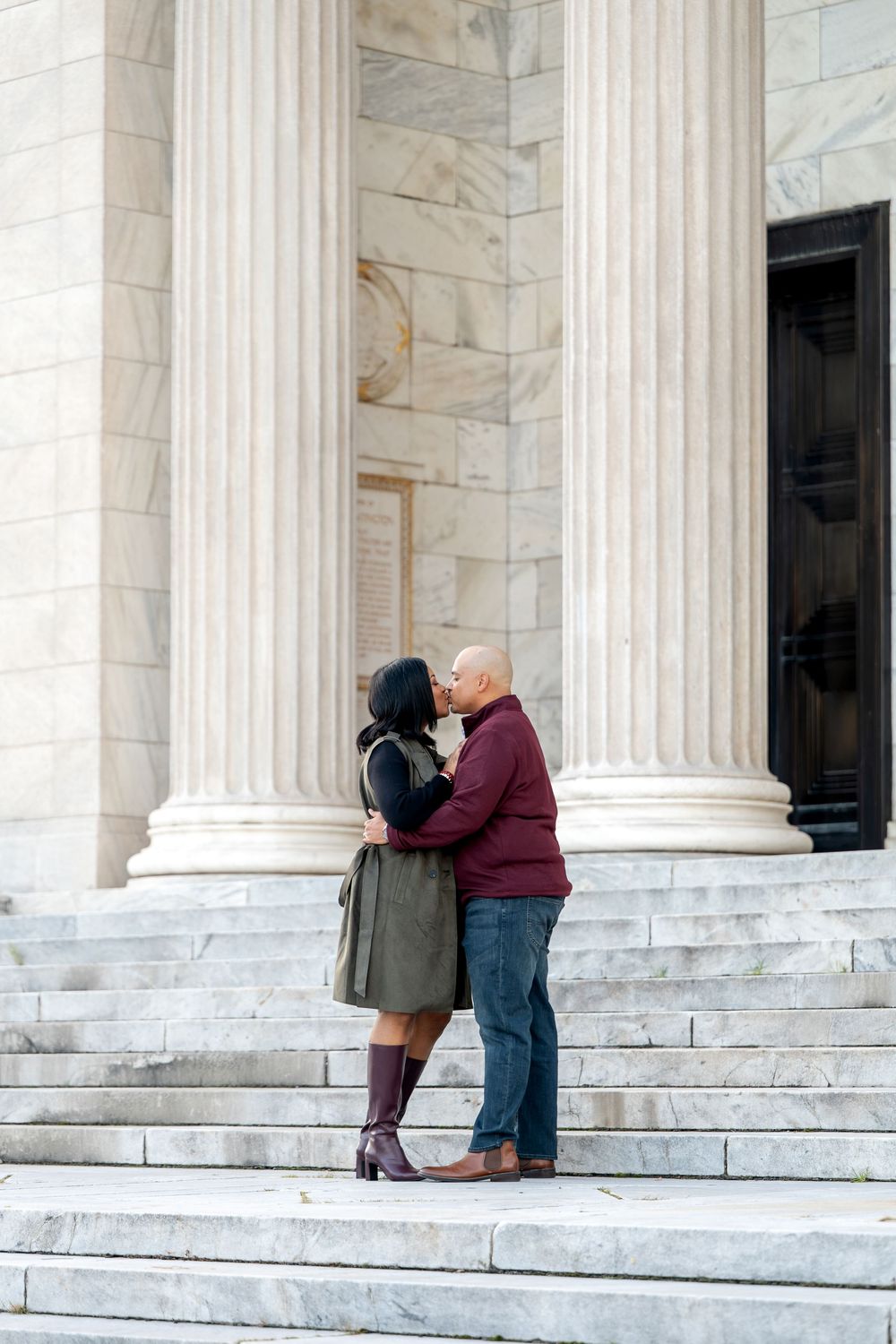 A couple shares a romantic kiss on the steps of a grand marble building with tall columns.