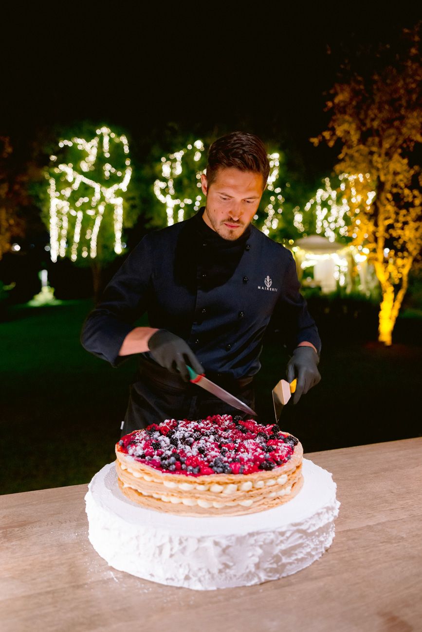 Baker assembling a millefoglie cake during an outdoor rehearsal dinner near Lake Garda