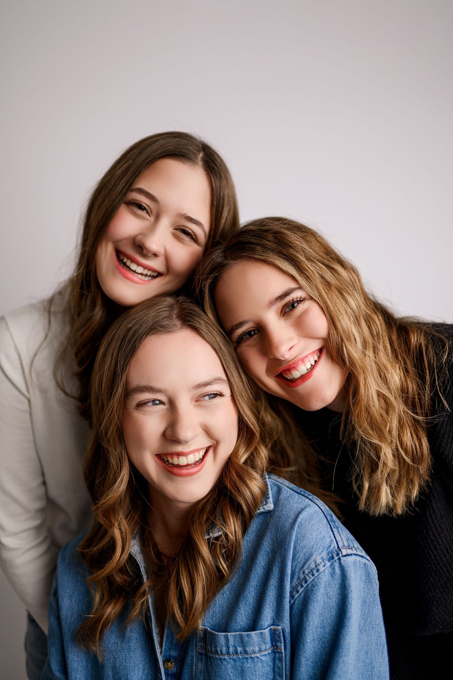 Three smiling young women posing together for a portrait photo against a white background.