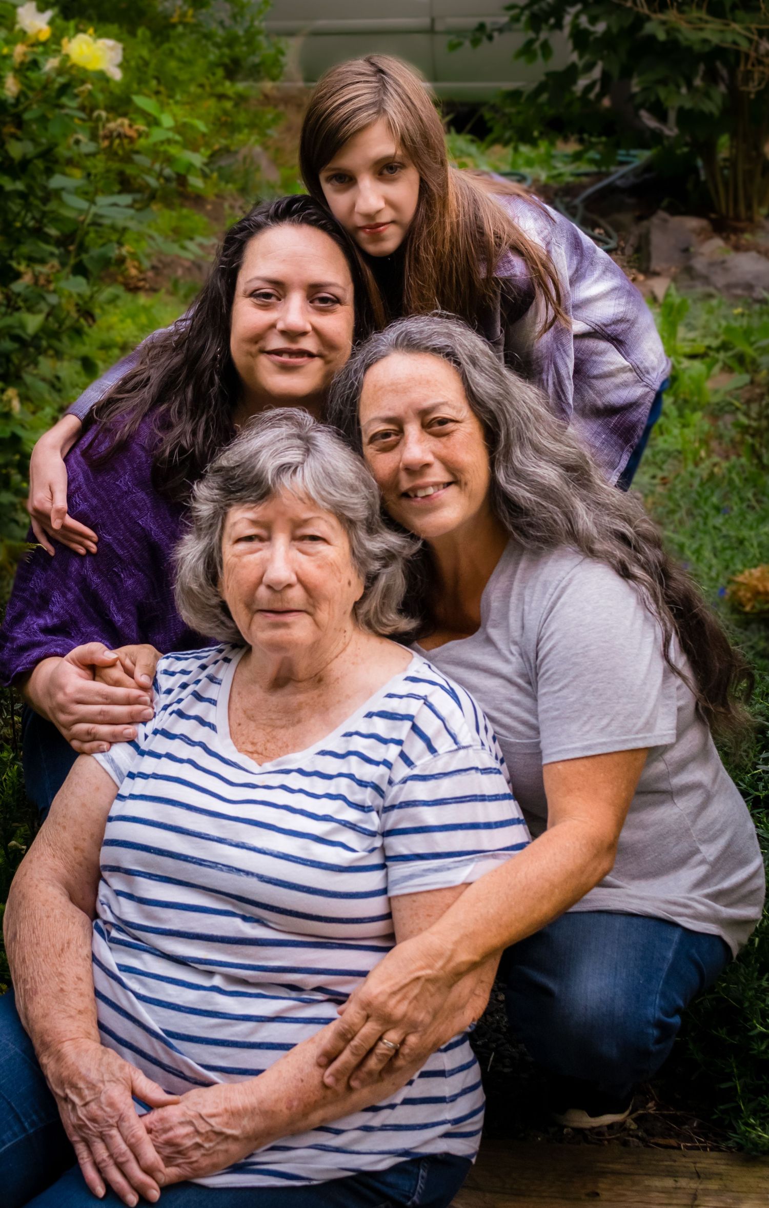 Four generations of women pose together outdoors, smiling warmly in a heartfelt family portrait.