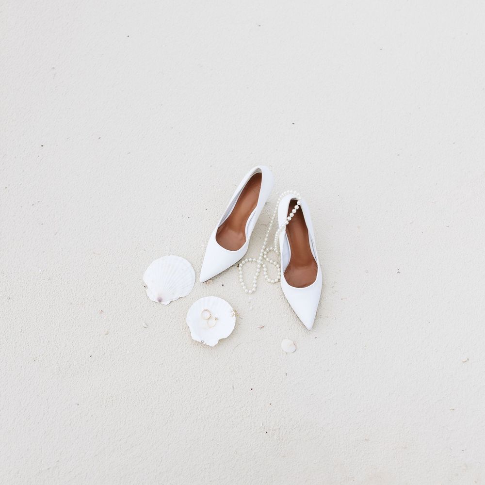 Minimal white objects including shoes and accessories arranged on a light neutral background.