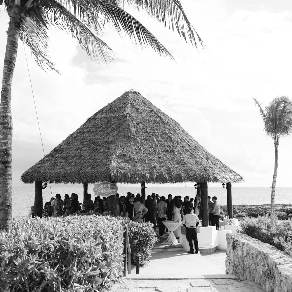 Black and white panoramic view of thatched roof huts along a tropical beachfront with palm trees.