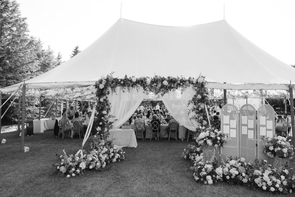 Elegant outdoor wedding tent adorned with floral arrangements and draped fabric entrance on a lush green lawn.