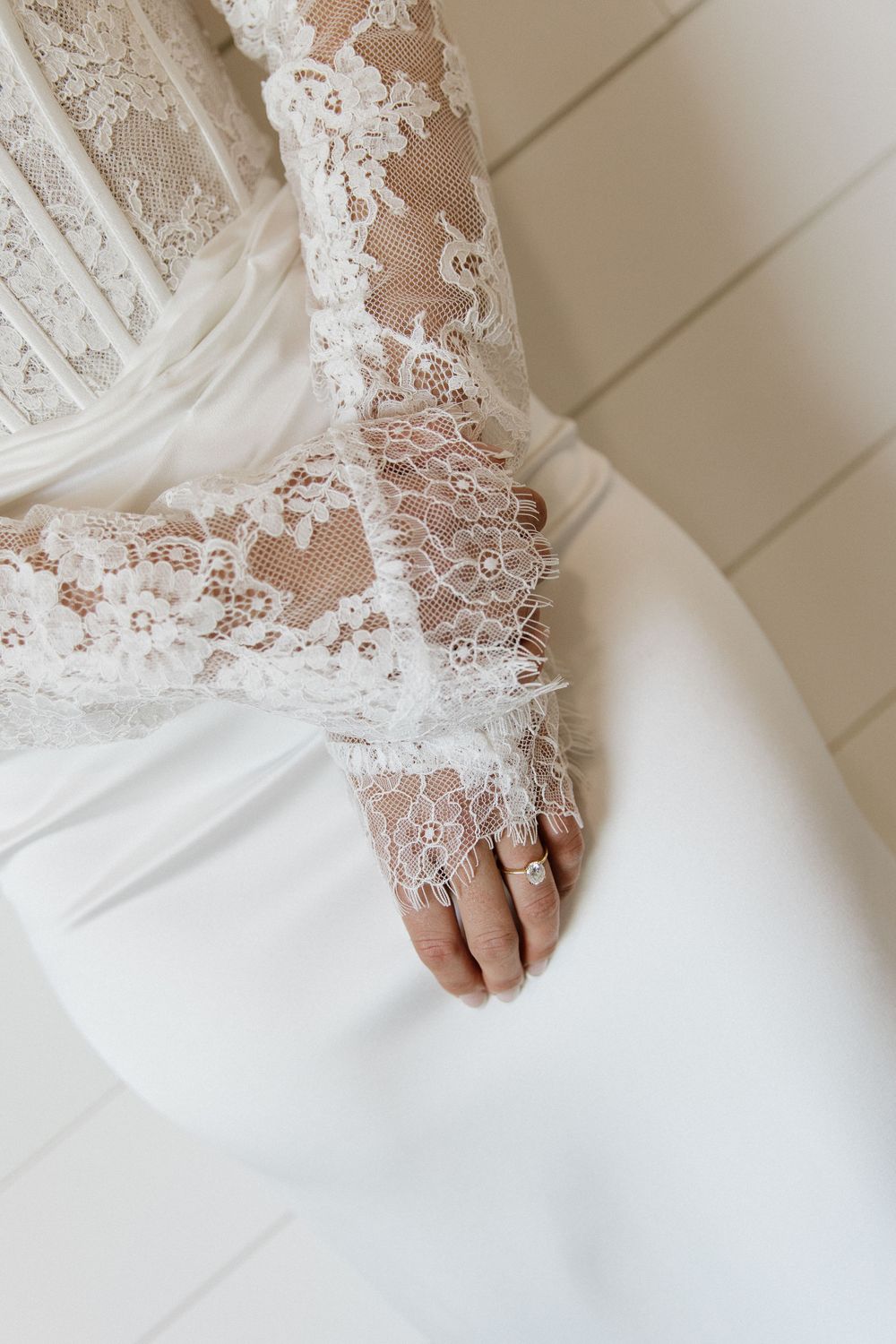 Close-up of a bride's lace long-sleeve wedding dress with delicate floral details and a gold ring on her hand.