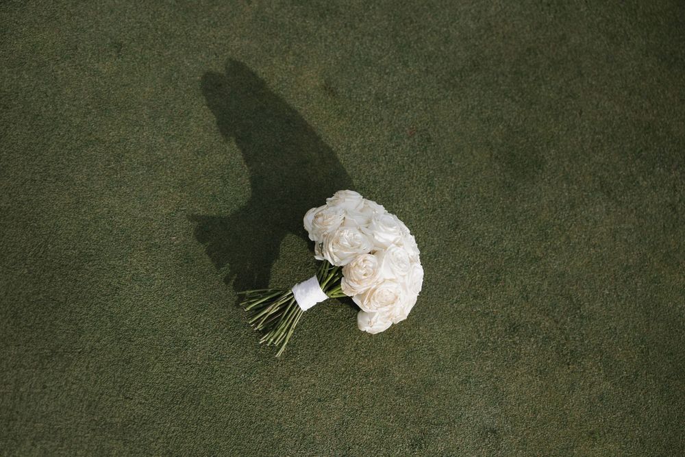 White bridal bouquet of roses lying on green grass with a soft shadow, perfect for wedding photography.