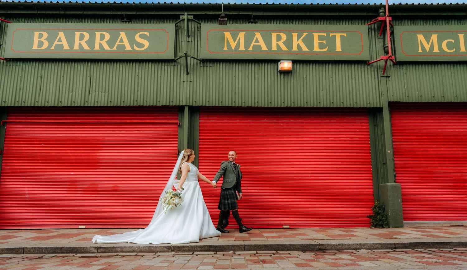 A dramatic black and white wedding photo showing a bride's flowing veil and dress on a city street in front of historic buildings.