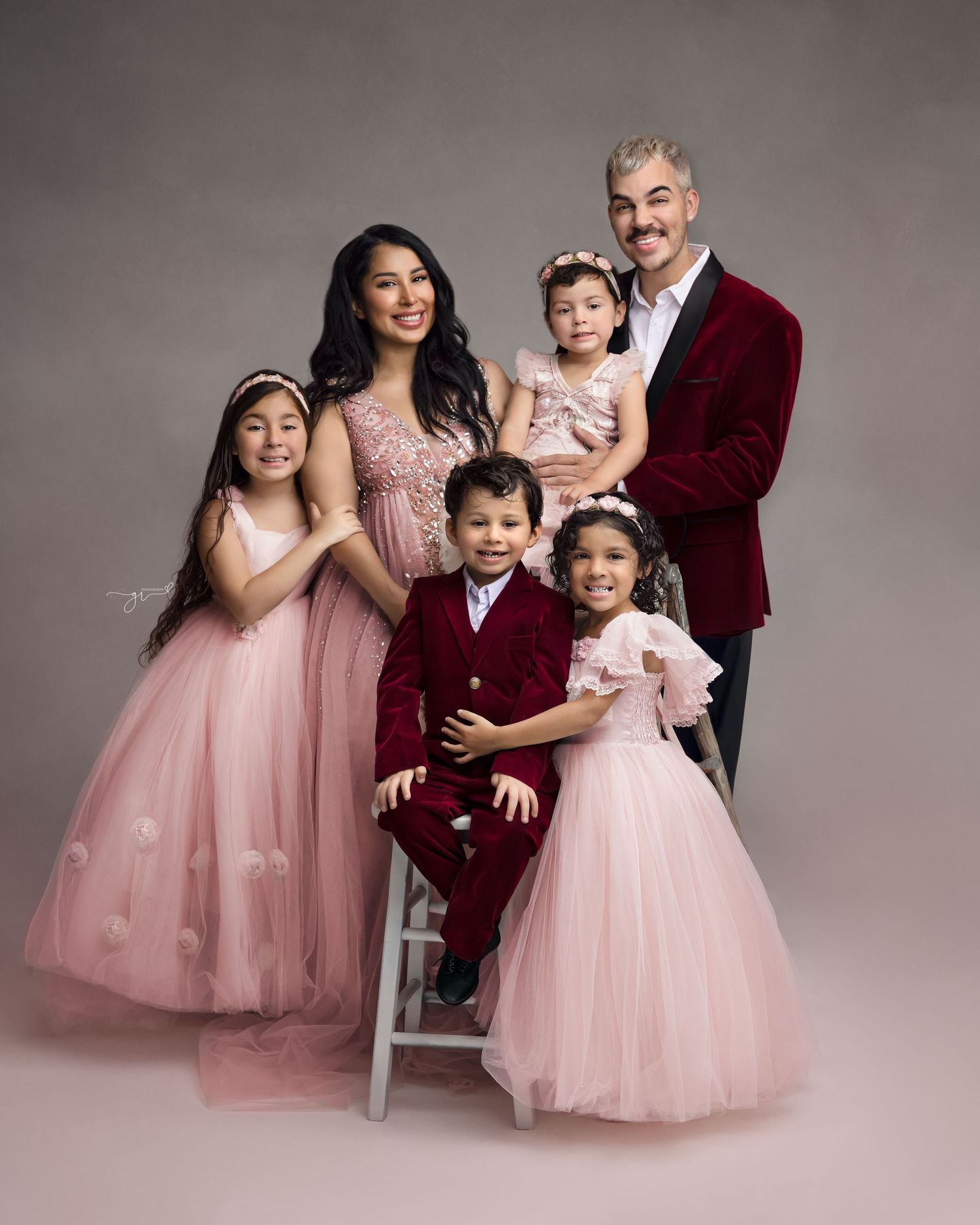 A family of five poses elegantly in coordinating pink and red formal attire for a professional studio portrait.