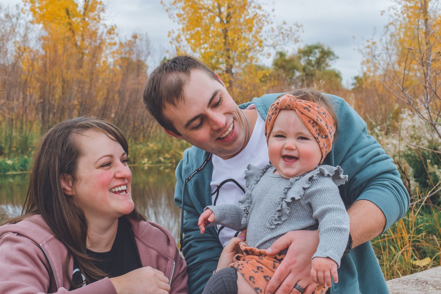 Happy family with two parents and a laughing baby outdoors in autumn park with colorful fall foliage.