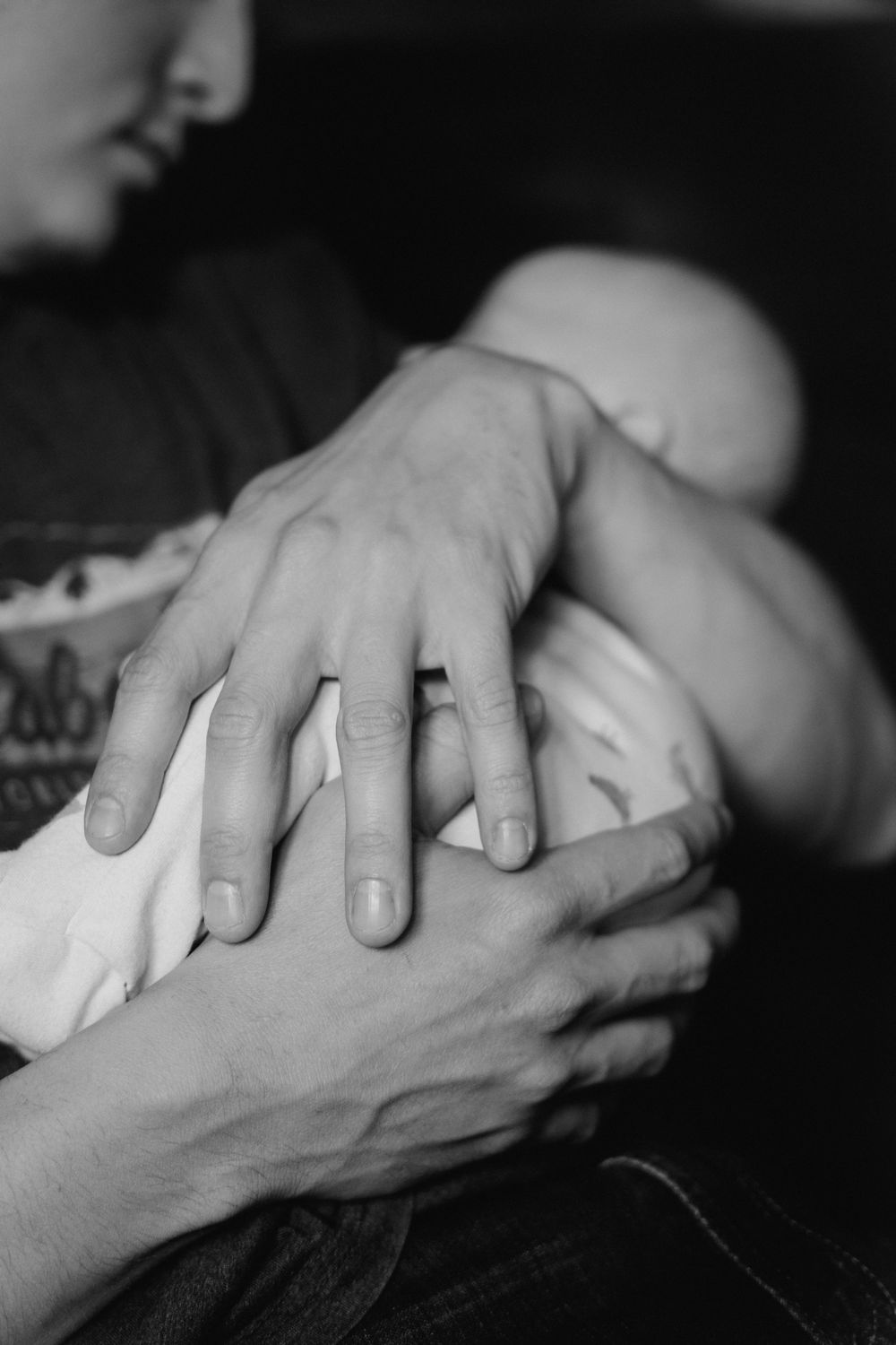 Black and white photo of a parent cradling a newborn baby, with a wedding ring visible on their hand.
