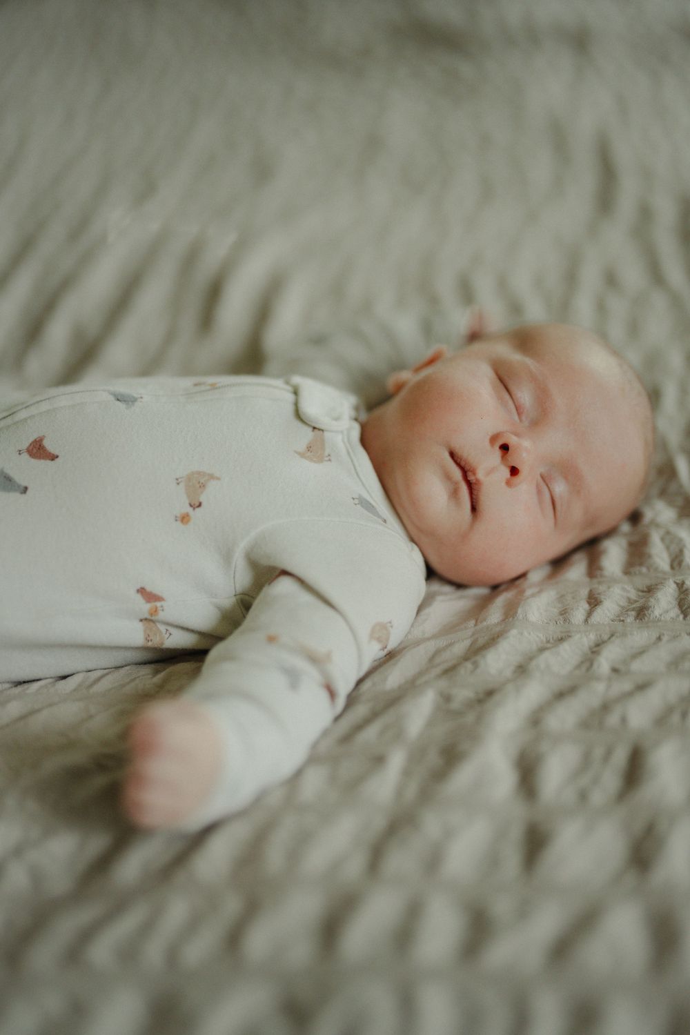 Peaceful newborn baby sleeping on a soft green blanket wearing a white printed onesie.
