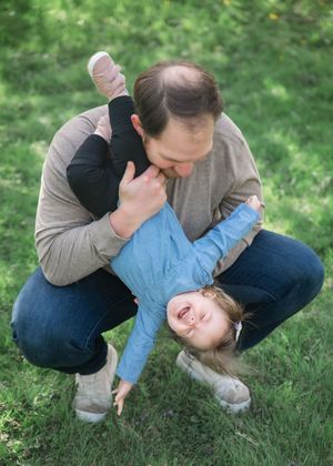 A father playfully holds his laughing child upside down on green grass outdoors.