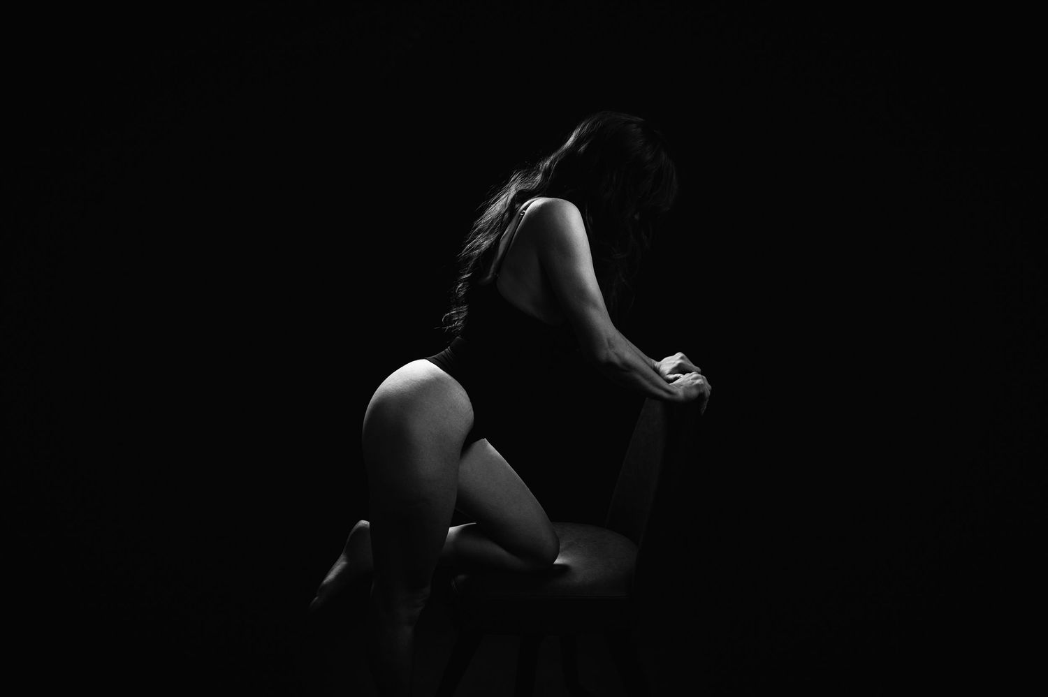Black and white silhouette of a woman sitting gracefully in dramatic low-key lighting against a dark background.