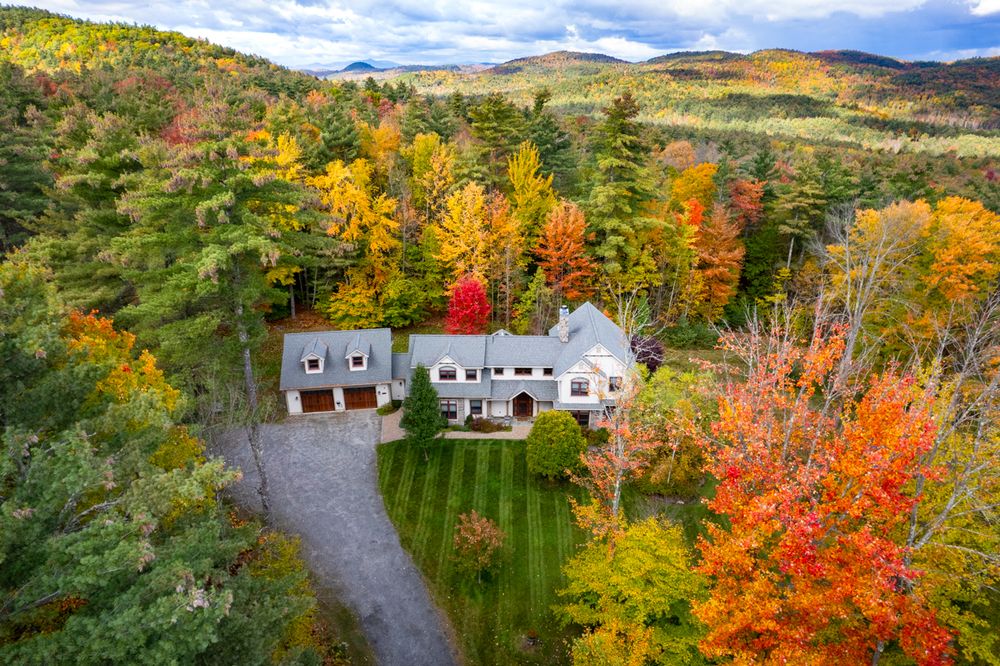 Aerial photo of a vacation rental in Bolton Landing surrounded by vibrant autumn foliage and rolling hills in a scenic rural landscape.