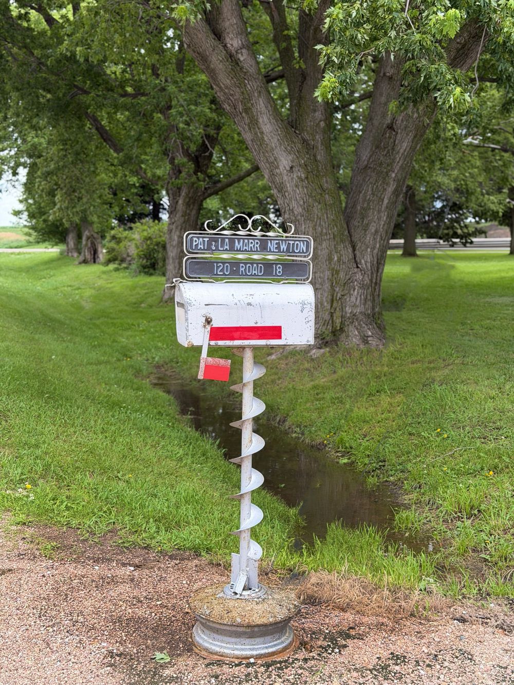 Creative mailbox mounted on an auger drill bit post with address sign for Pat La Marr Newton at 120 Road 18.