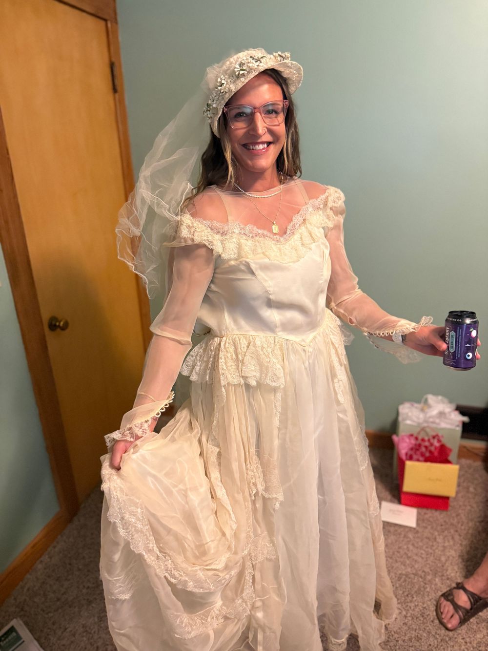 Woman in vintage white lace wedding dress and veil with safety glasses holding a can indoors.