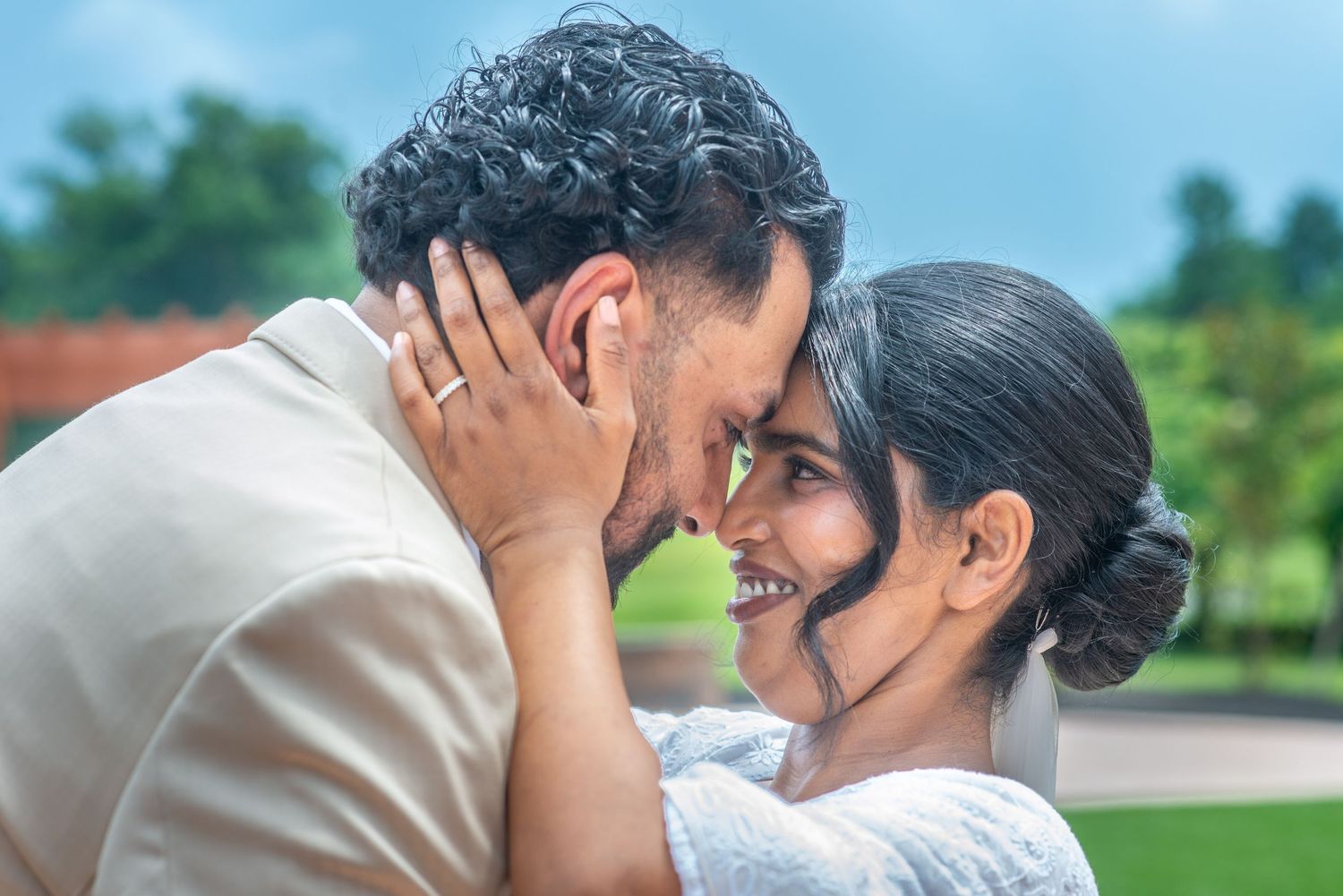 Romantic couple sharing an intimate moment outdoors, smiling and touching foreheads in a loving embrace.