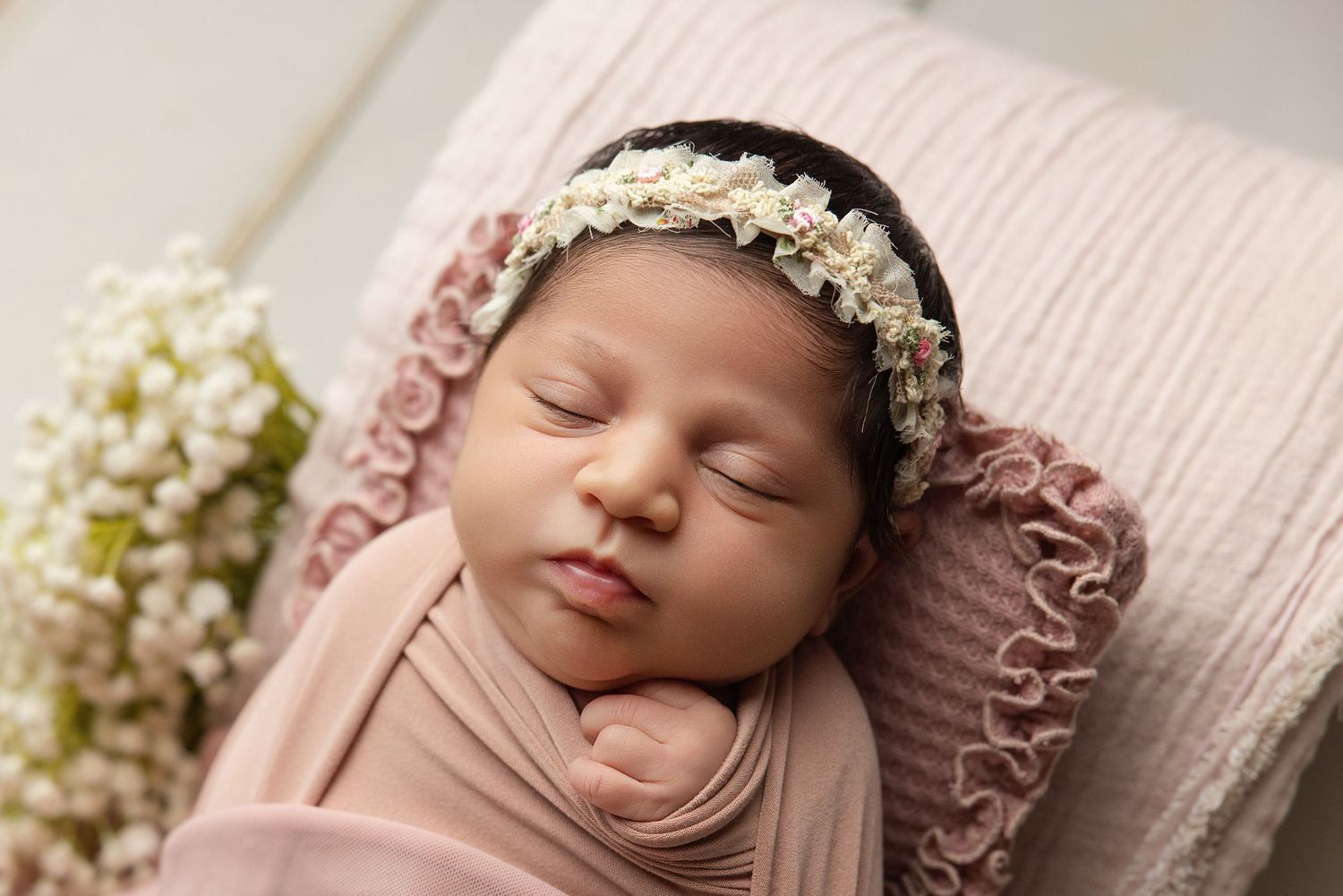 Sleeping newborn baby wrapped in teal swaddle inside a small bucket with a green pillow.
