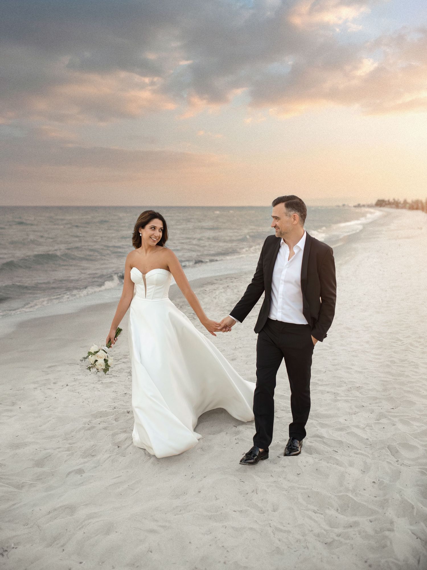 Candid wedding photography of a bride and groom holding hands and walking on a sandy beach at sunset.
