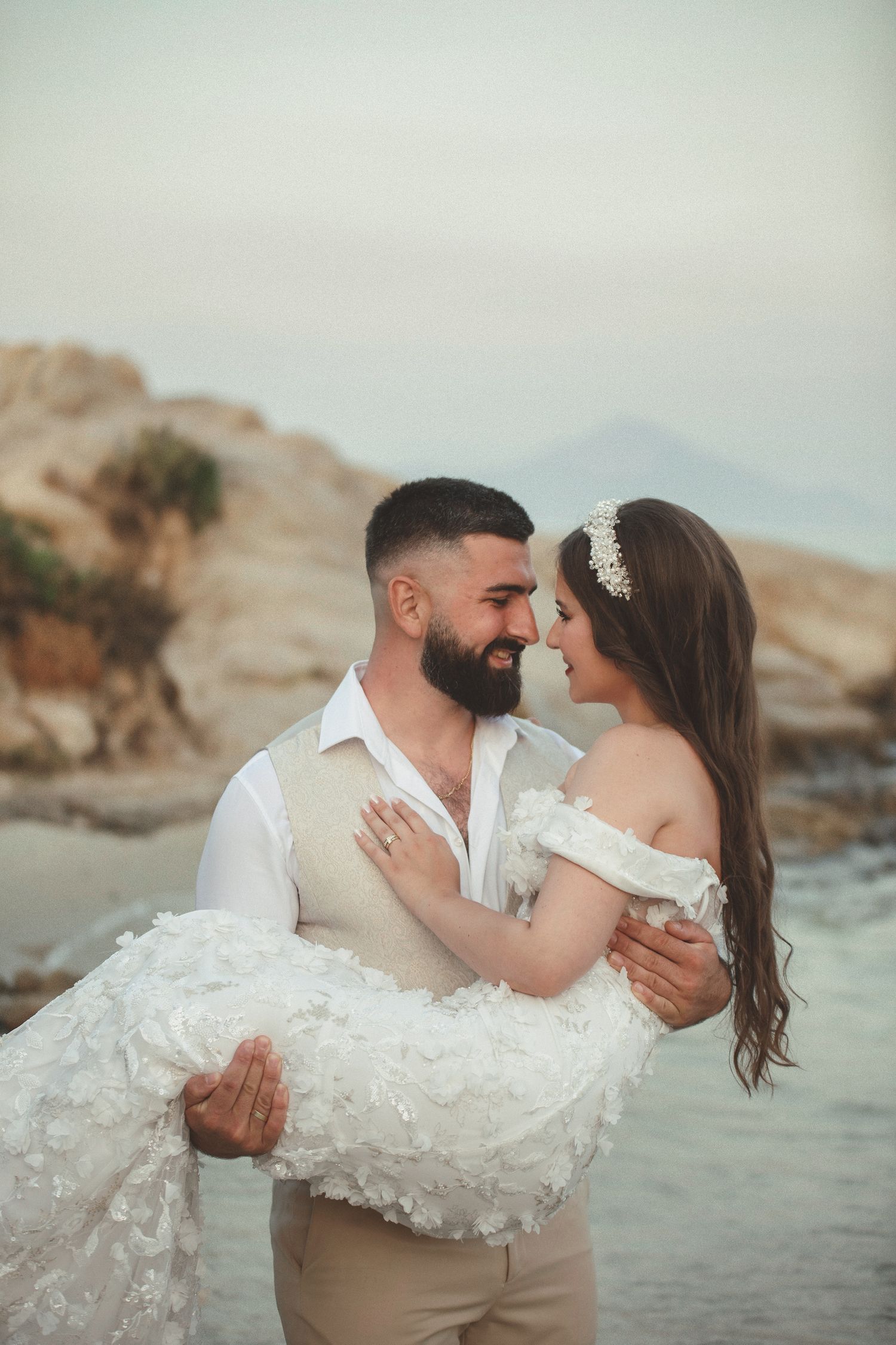 Documentary style wedding photo featuring a close-up portrait of newlyweds sharing a tender look on a sandy beach in Greece.