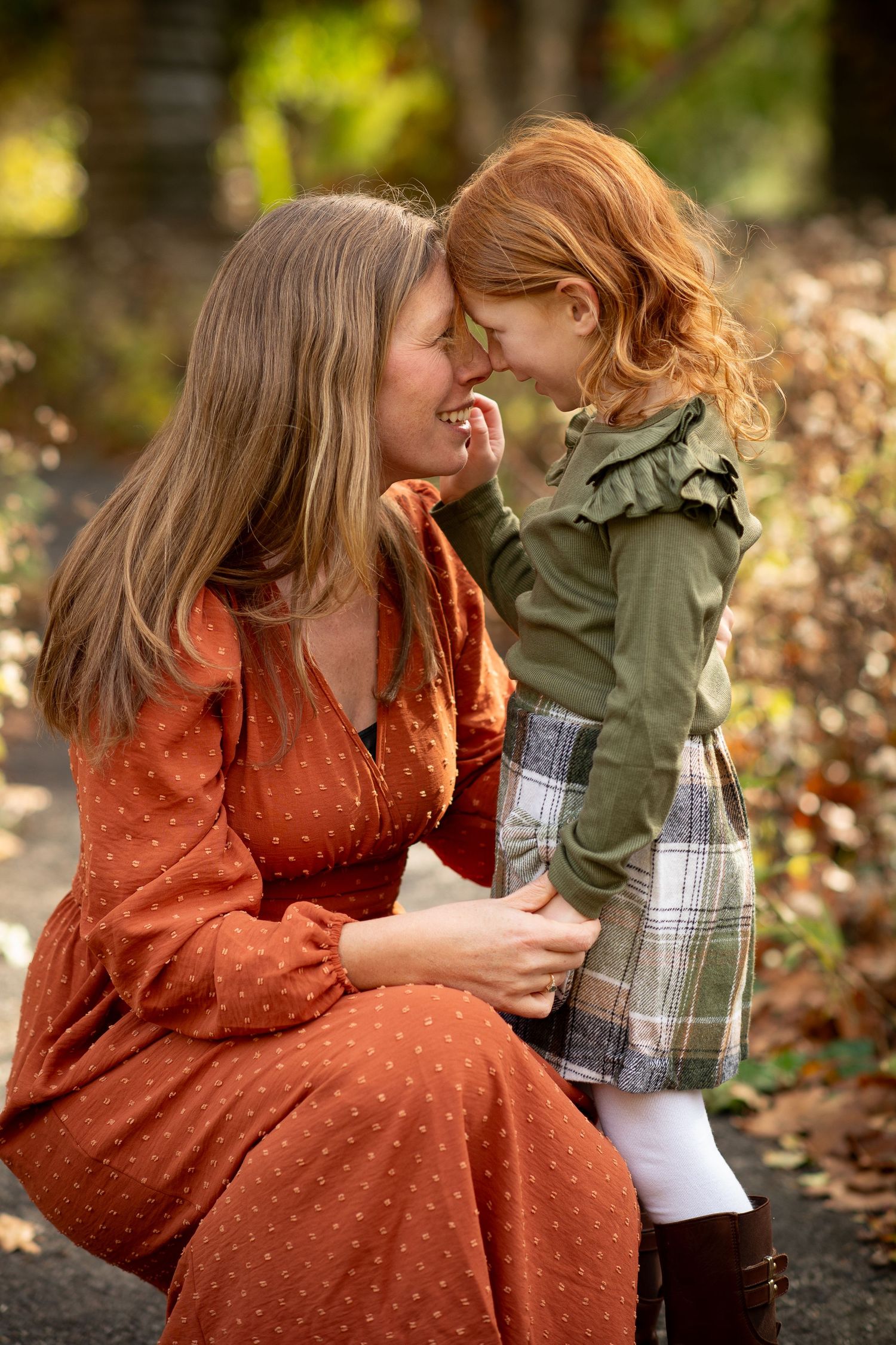 A mother and young redhead girl touch noses affectionately outdoors in autumn.