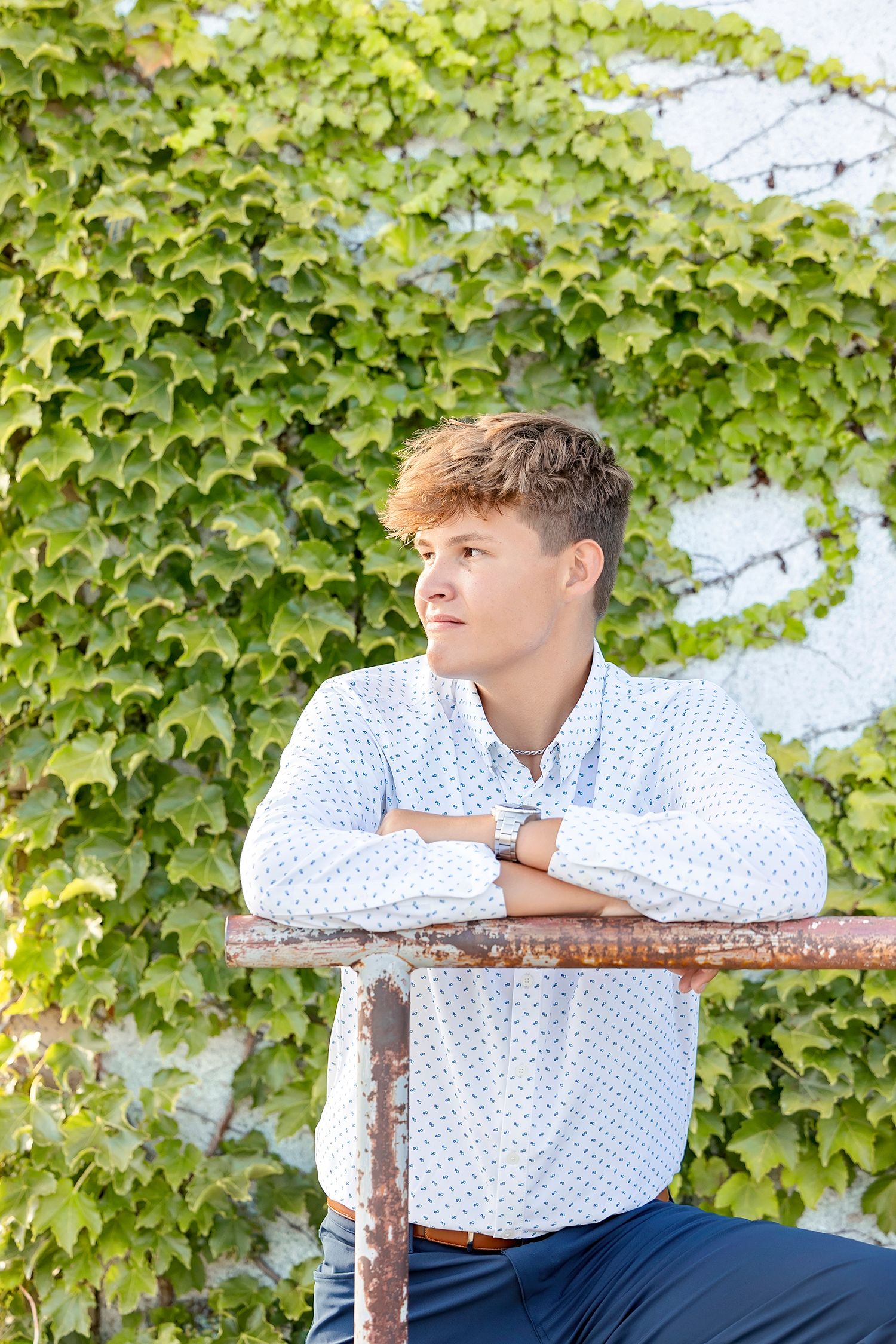 High school senior boy posing by an ivy-covered wall during a downtown senior photography session in Clear Lake, Iowa.
