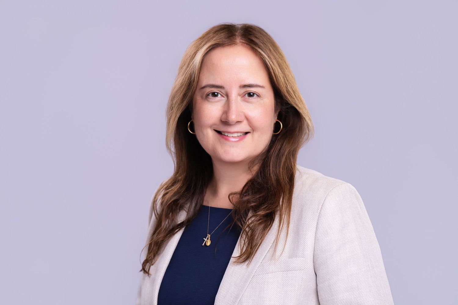 Professional woman in white blazer and navy top smiling confidently against a light gray background.