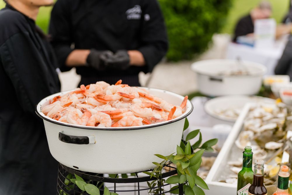 A large white bowl filled with fresh shrimp displayed at an outdoor catered seafood buffet event.