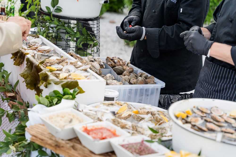 Chefs in black gloves serve fresh oysters and seafood at an elegant outdoor catering buffet table.
