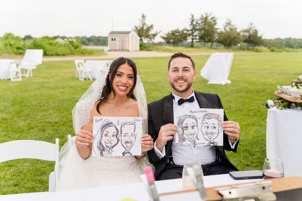 Bride and groom holding caricature drawings at outdoor wedding reception on green lawn.